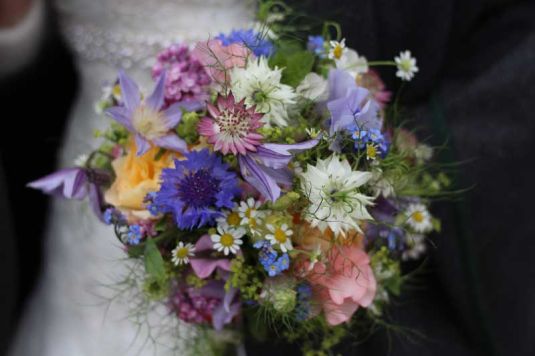 Brautpaar hält einen bunten Wiesenblumenstrauss mit Kornblumen, Margeriten und Wildblumen in der Hand