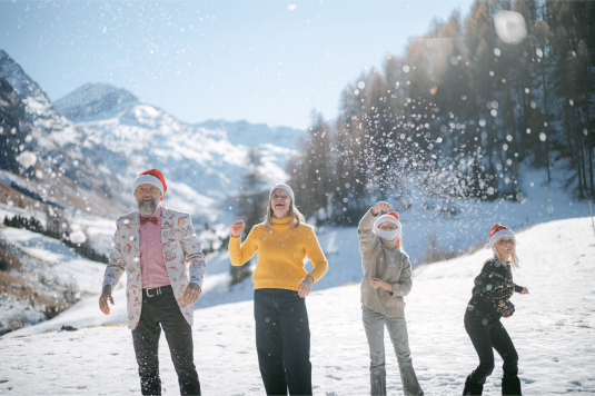 Familie Witschi beim ausgelassenen Schneespiel im Fextal — mit Weihnachtsmützen und strahlenden Gesichtern vor imposanter Bergkulisse