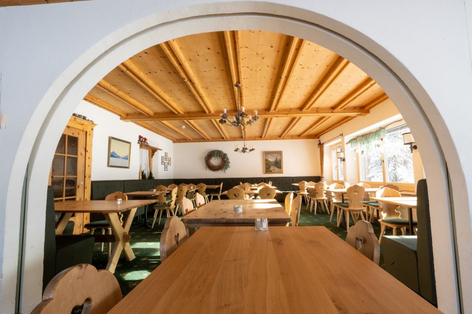Blick durch einen weissen Rundbogen in den Speisesaal der Sonne Fex mit Holzdecke, traditionellen Engadiner Stühlen und Berggemälden an den Wänden